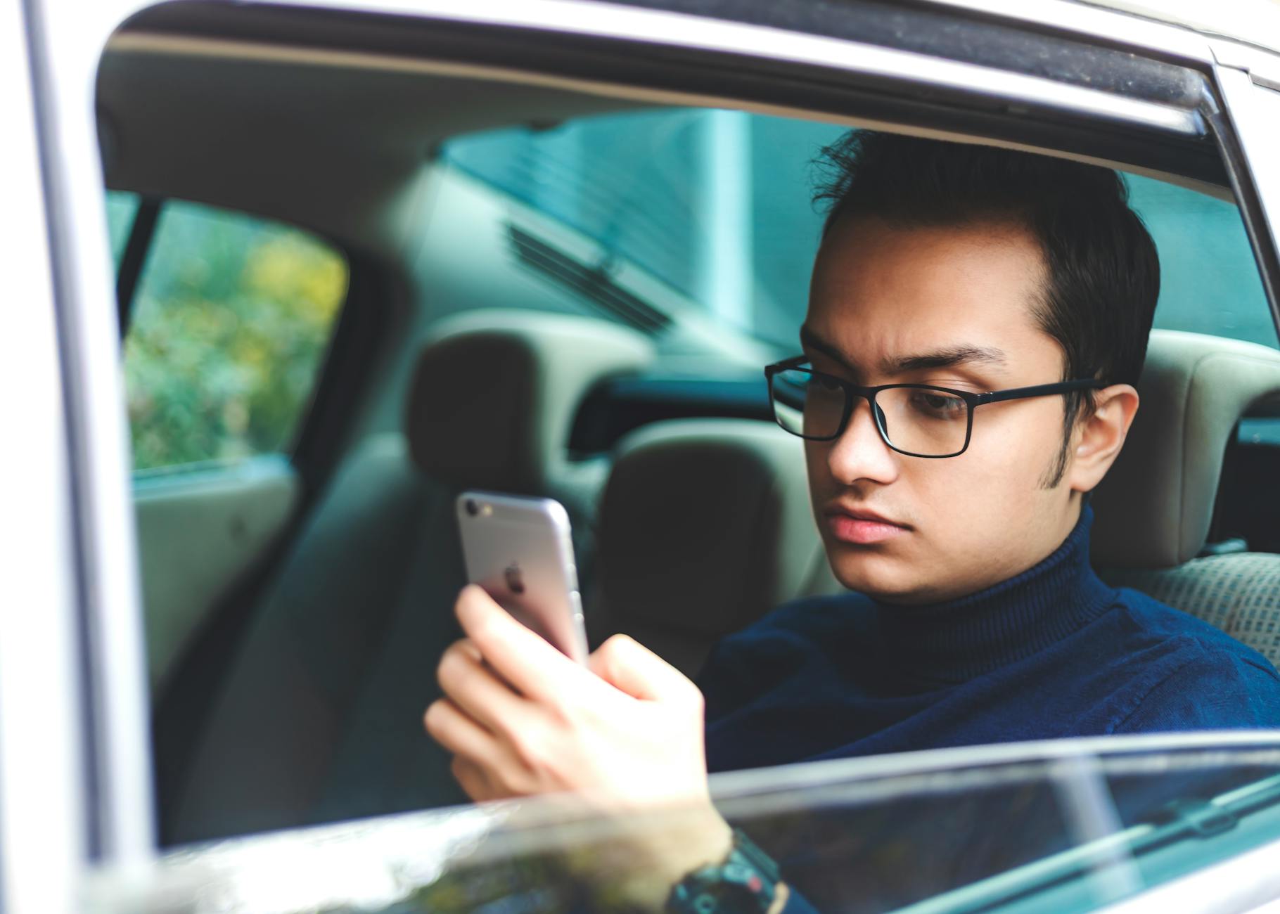 Mężczyzna w okularach korzysta ze smartfona w zaparkowanej Hondzie