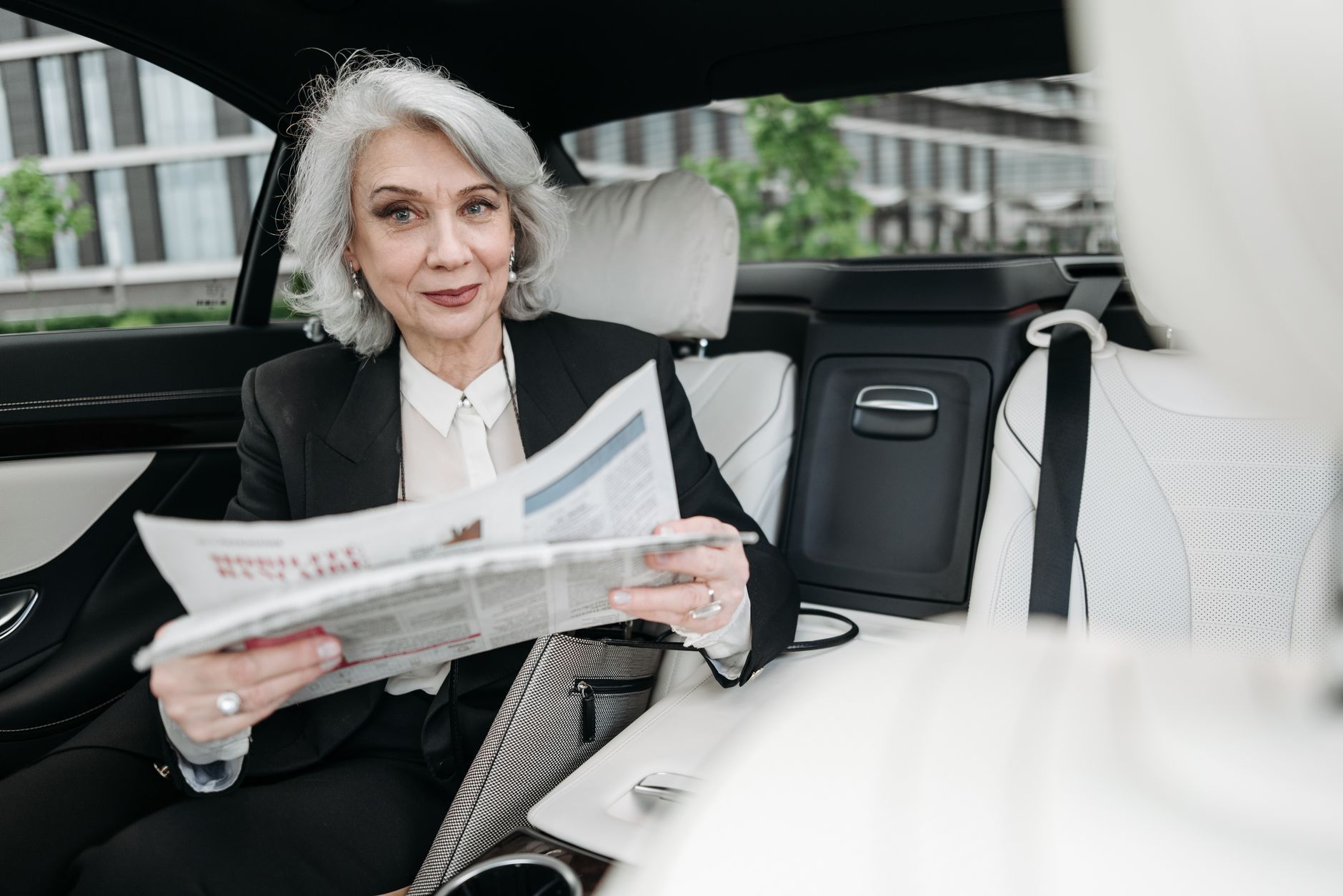 Starsza kobieta biznesu czyta gazetę w zaparkowanym Porsche