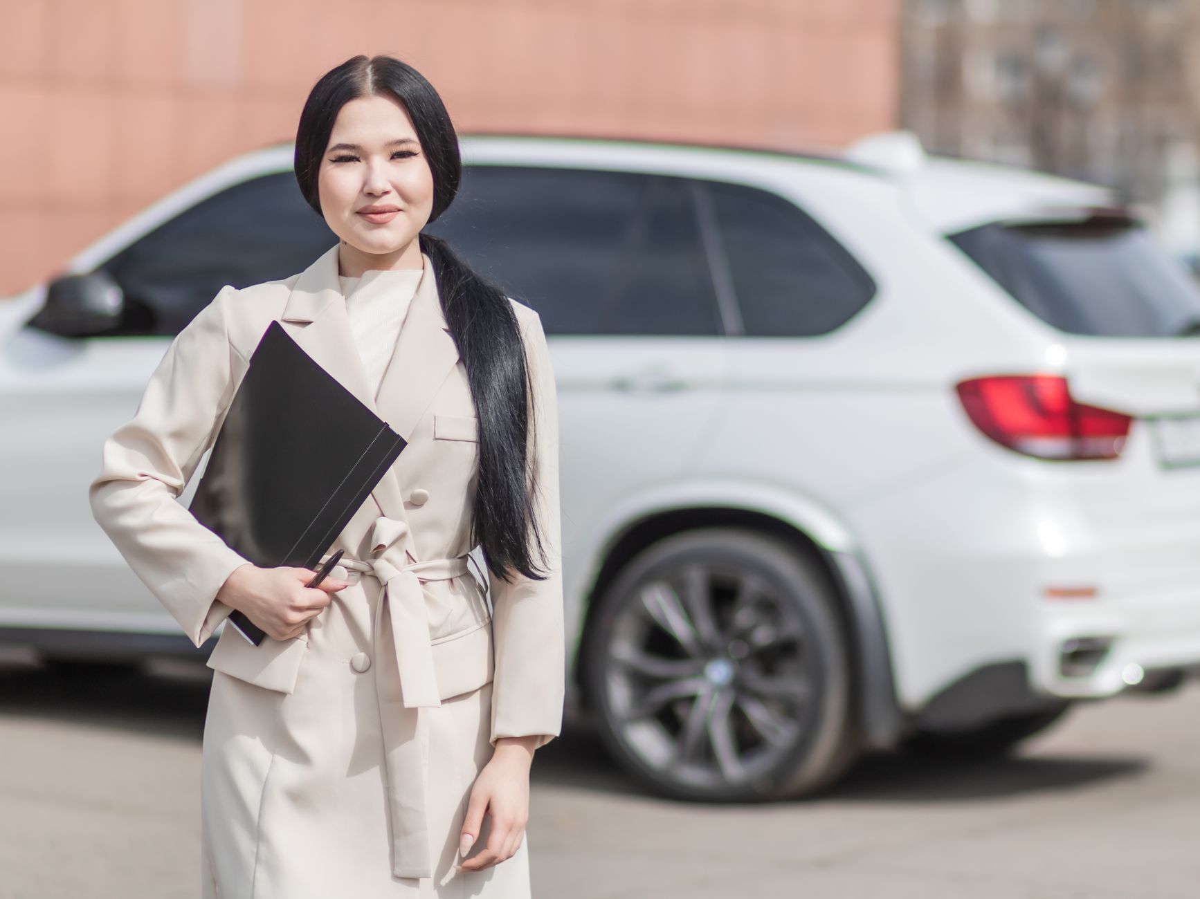 Uśmiechnięta kobieta w biznesowym stroju stoi przy luksusowym Porsche